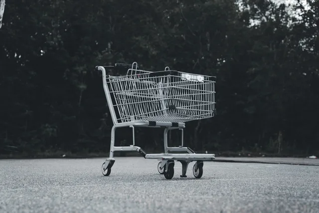 A lone shopping cart sits abandoned on a deserted street with a dark forest backdrop. Weniger Warenkorbabbrüche auf der Checkout-Seite